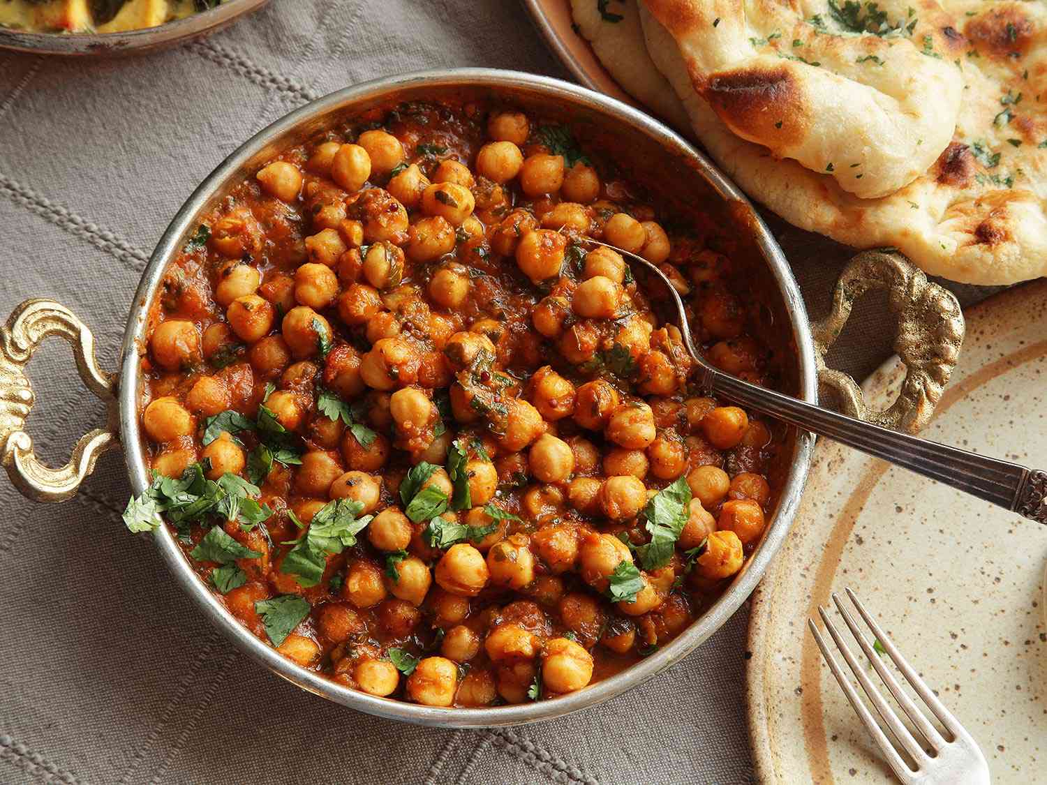 A close-up of a steaming bowl of chana masala, garnished with fresh coriander leaves and a wedge of lemon, inviting a sensory journey through the vibrant flavors of Indian cuisine.