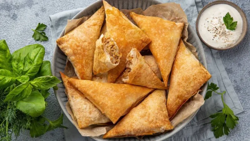 A plate of golden, crispy samboosa filled with spiced meat and served with a side of mint chutney